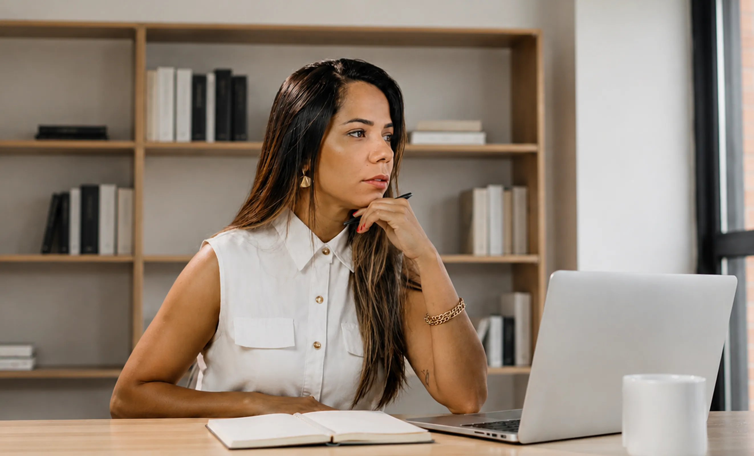 Mujer profesional reflexionando frente a su laptop en un espacio de trabajo